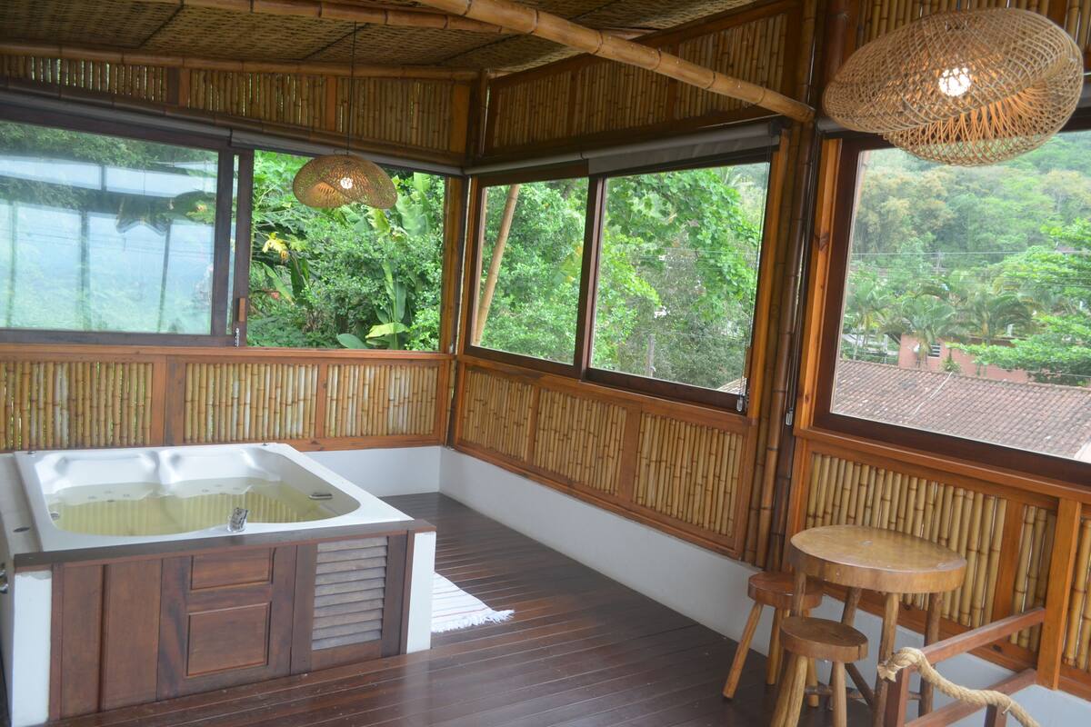 Una habitación con piso de madera, un ventanal amplio, pared de bambú, una mesa de madera y una silla de madera.