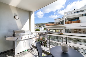 A balcony with a grill, a table, and a view of buildings.