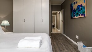 A bedroom with a large bed, a wardrobe, a painting, and a lamp. - Flatrock 909 (Cape Town)