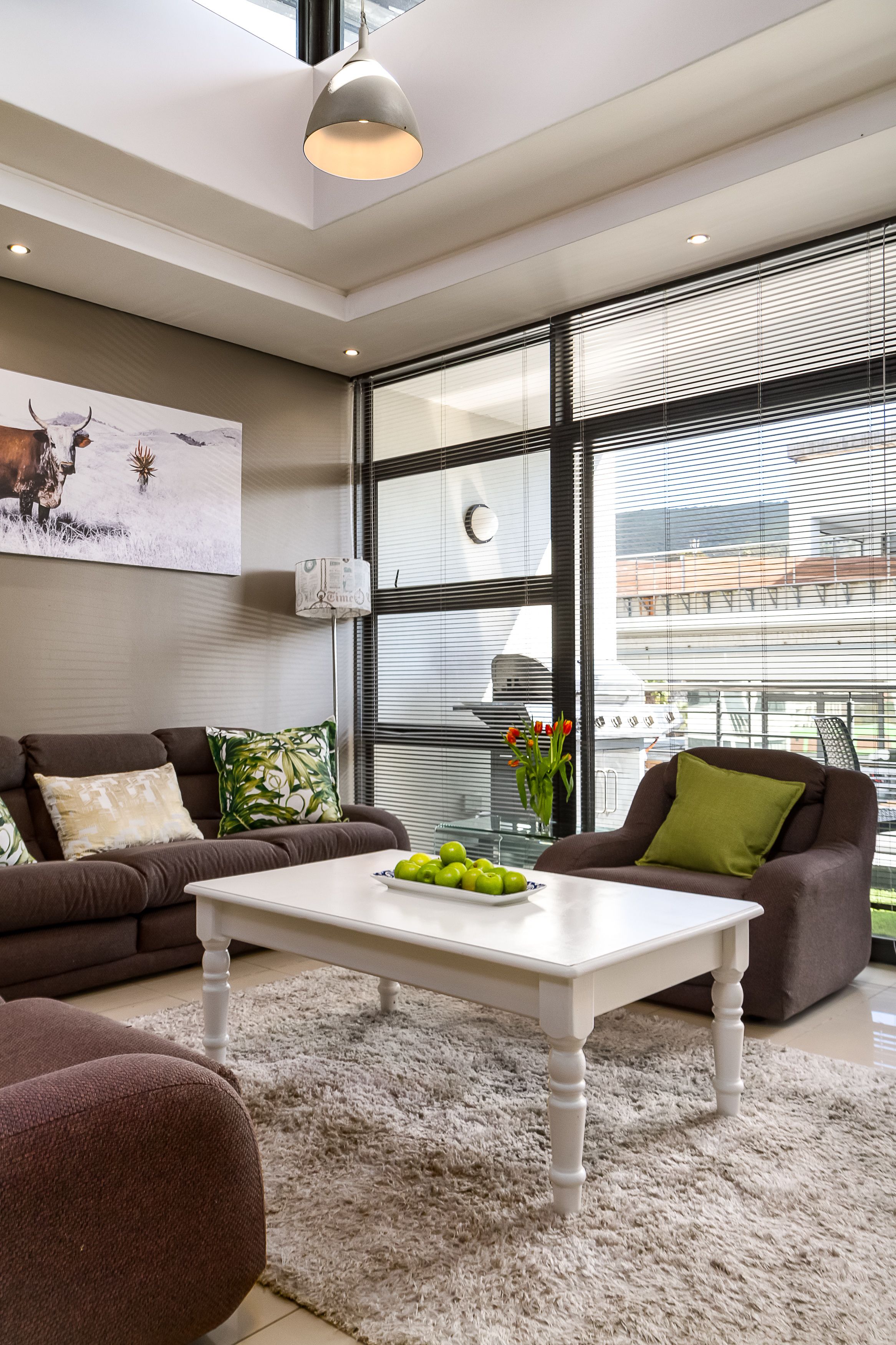 Un salon moderne avec un canapé, une table basse et une grande fenêtre équipée de stores.