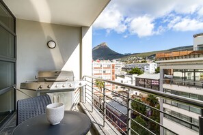 A balcony with a grill, a table with a bowl, and a view of a mountain and buildings.