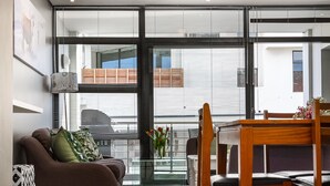 A modern living room with a sofa, dining table, chairs, and a hanging light fixture. - Flatrock 909 (Cape Town)