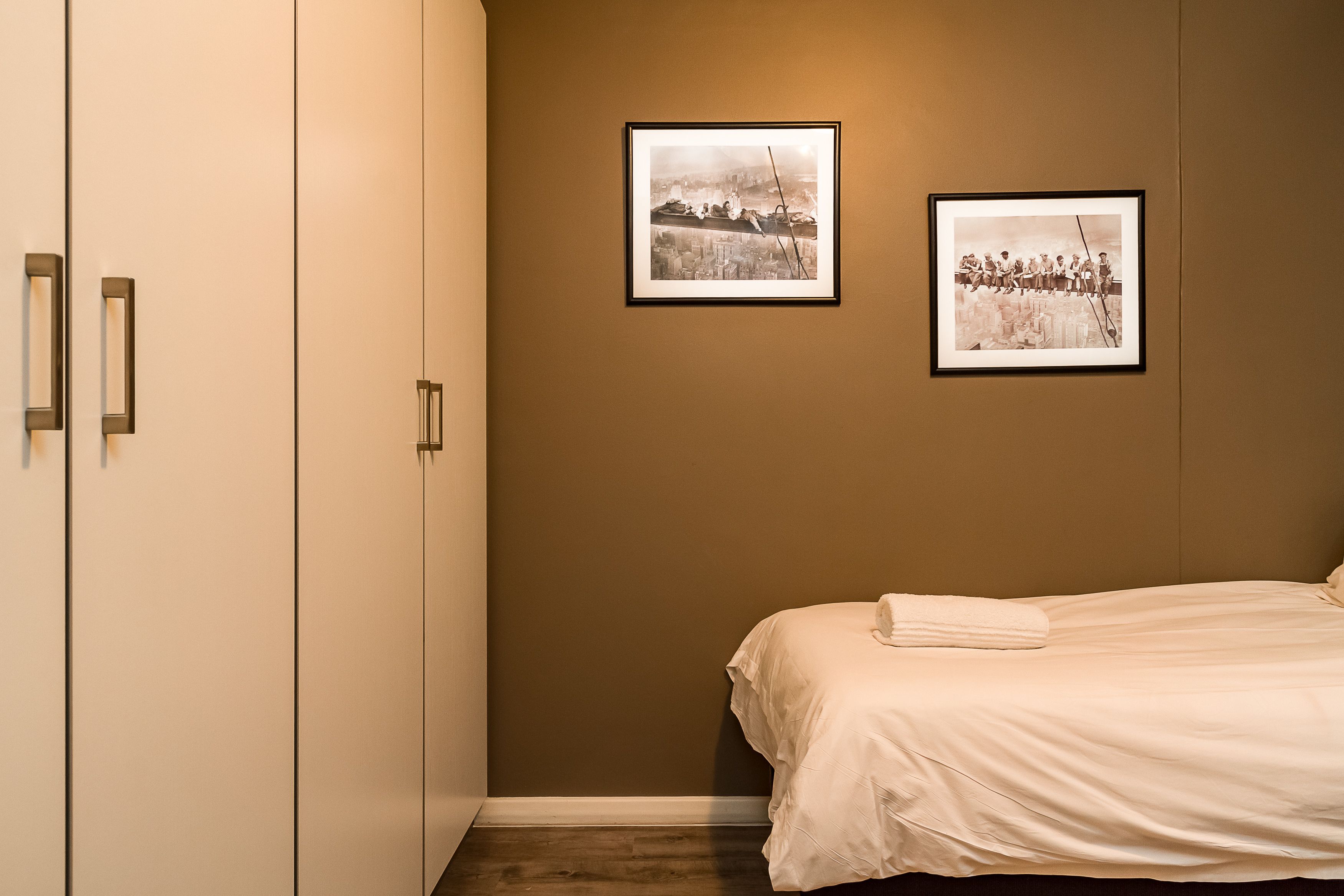 A bedroom with a bed, a wardrobe, and two framed pictures on the wall.