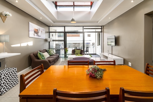 A modern living room with a wooden dining table, a sofa, and a TV.