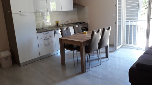A modern kitchen with white cabinets, a wooden dining table, and two chairs. - Apartments Juliet (Orebic)