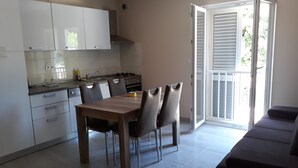 A modern kitchen with white cabinets, a dining table with chairs, and a sliding glass door leading to a balcony. - Apartments Juliet (Orebic)