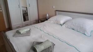 A neatly made bed with white bedding and teal trim, a grey towel on the bed, and a white wardrobe with a mirror. - Apartments Juliet (Orebic)