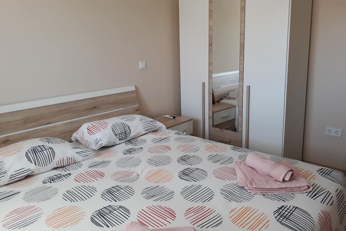 A bedroom with a bed, a wooden headboard, a bedside table, a mirror, and a wardrobe.