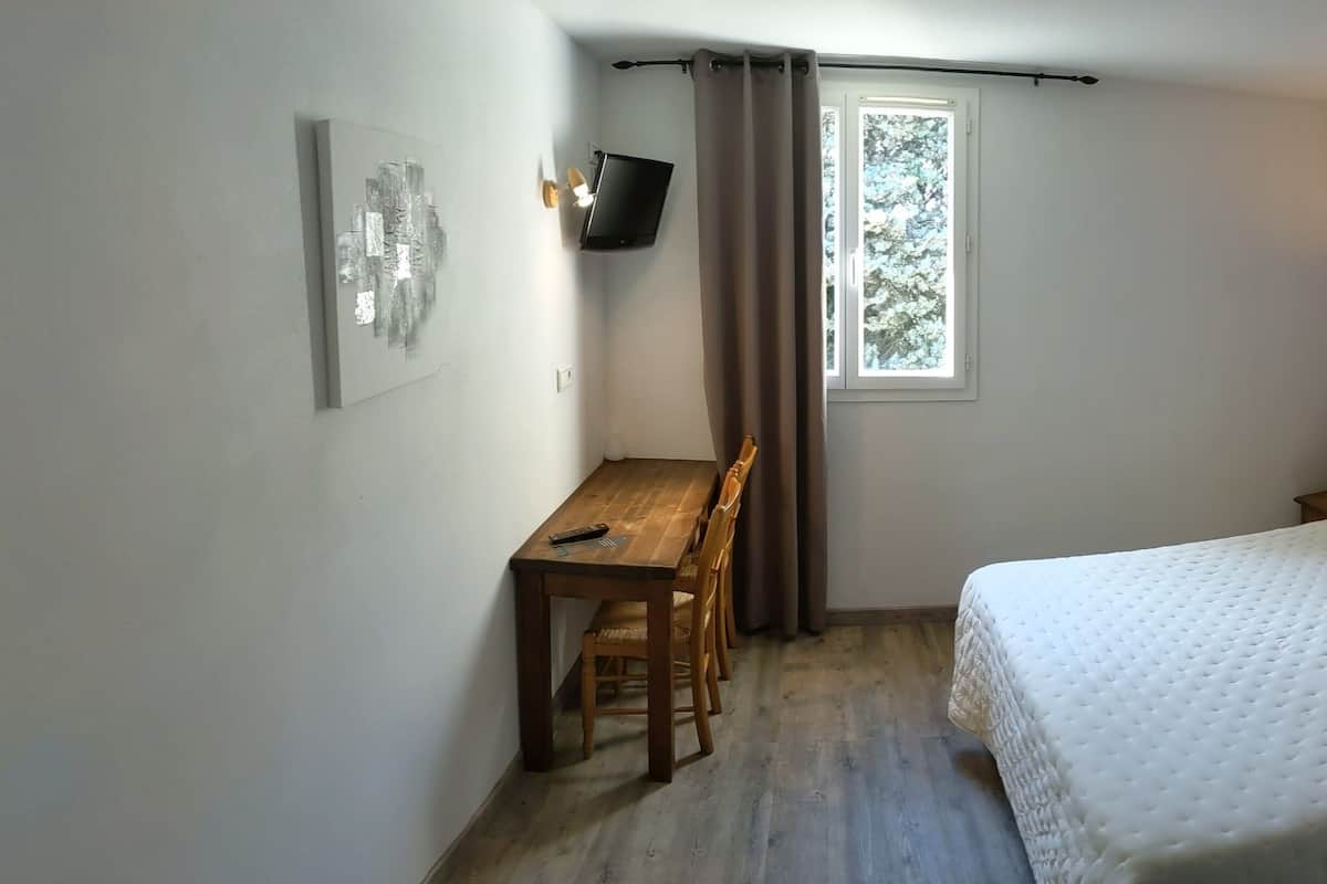 A bedroom with a bed, a desk, and a window.