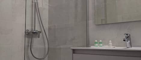 Un baño moderno con cabina de ducha de vidrio, tocador con espejo y lavamanos.