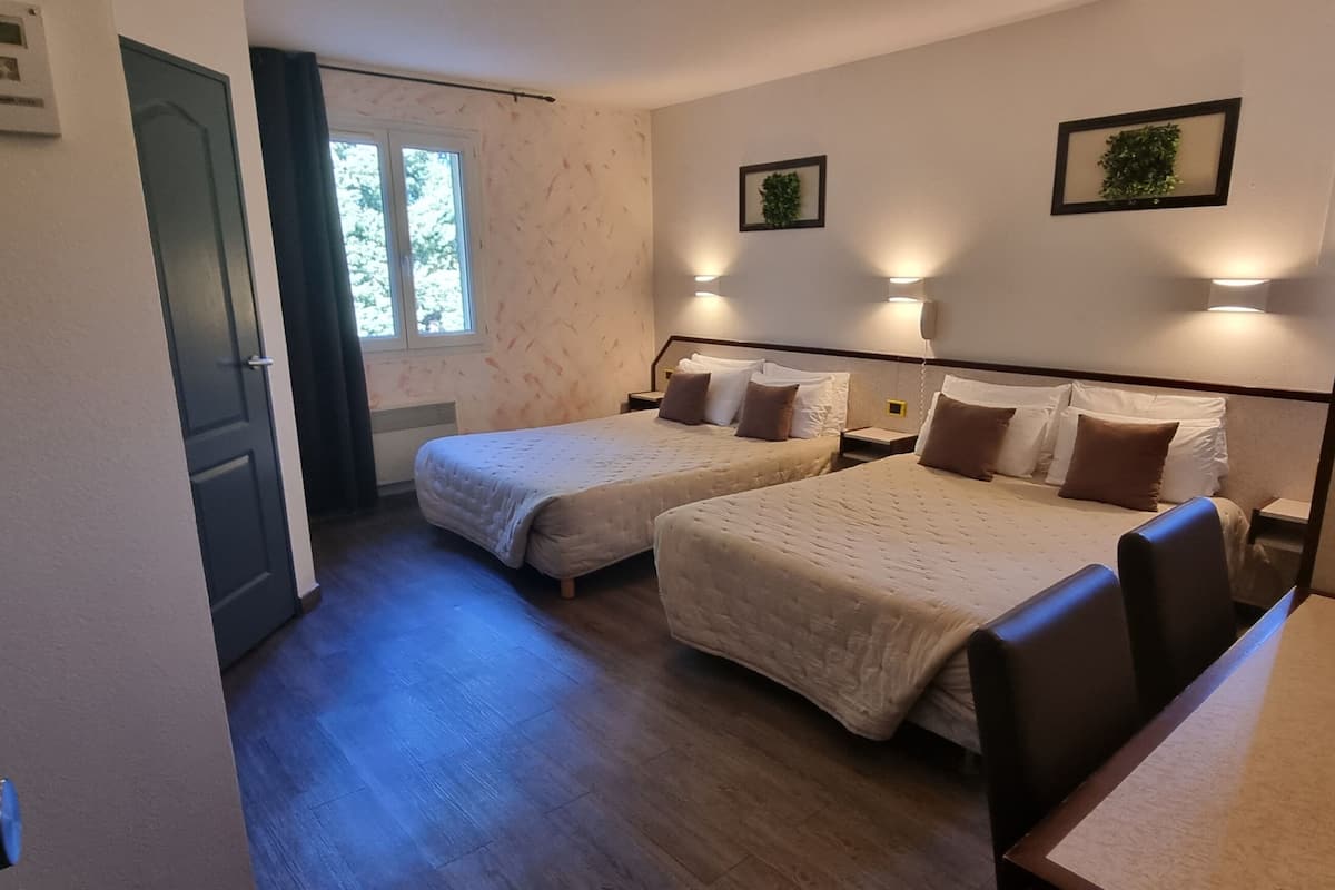 A hotel room with two beds, a desk, a chair, a window, and wall-mounted lights.