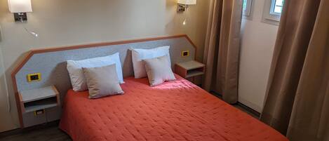 A hotel room with a large bed, two bedside tables, a wall-mounted lamp, and a framed artwork above the bed.