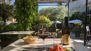 An outdoor dining area with a table set for a meal, including a bottle of wine, a basket of bread, and a variety of meats and cheeses. - Le Pradet Hotel (Vacqueyras)