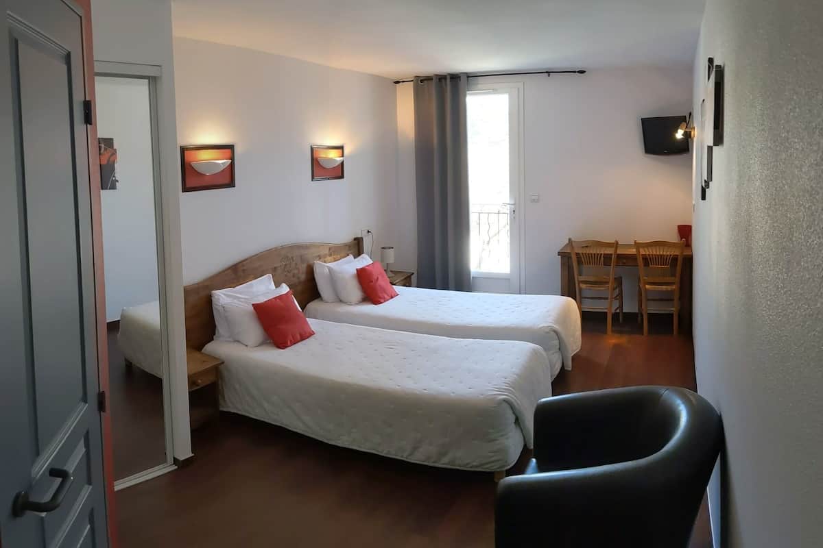 A hotel room with two beds, a desk, a chair, a TV, and a window with curtains.