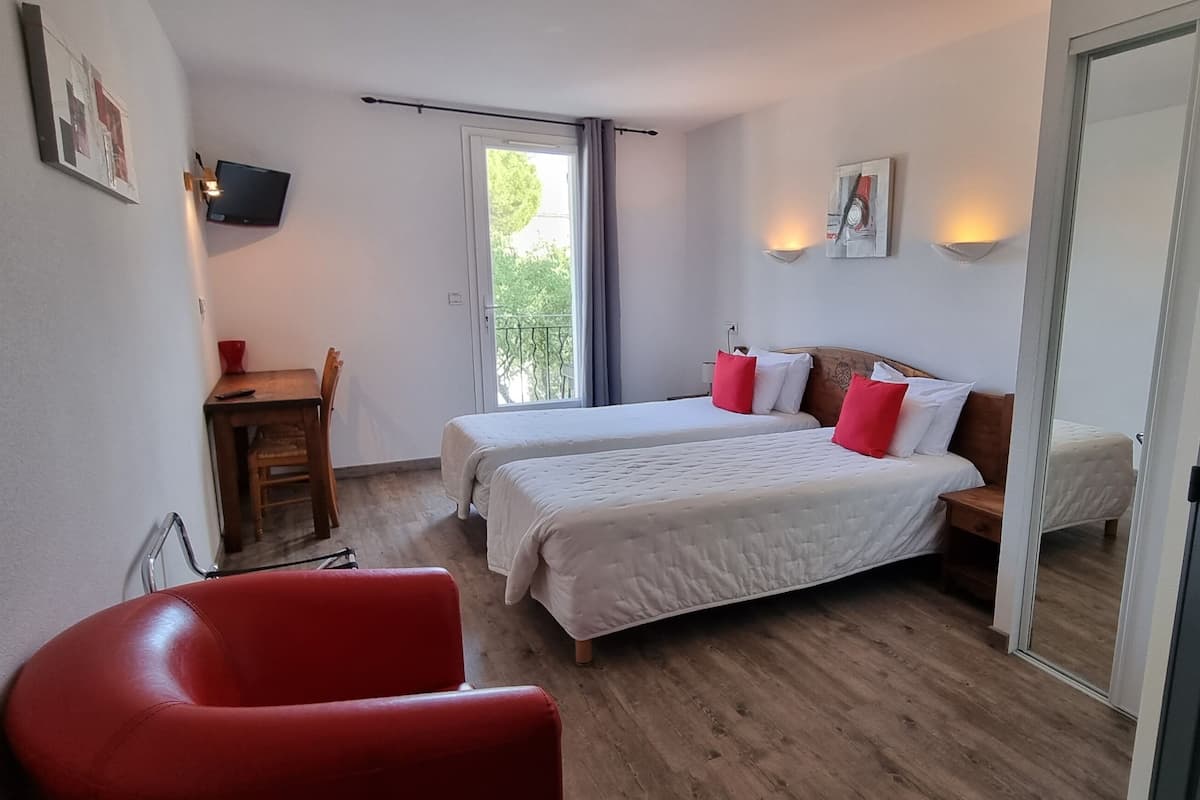 A room with two beds, a red chair, a wooden desk, and a TV on the wall.
