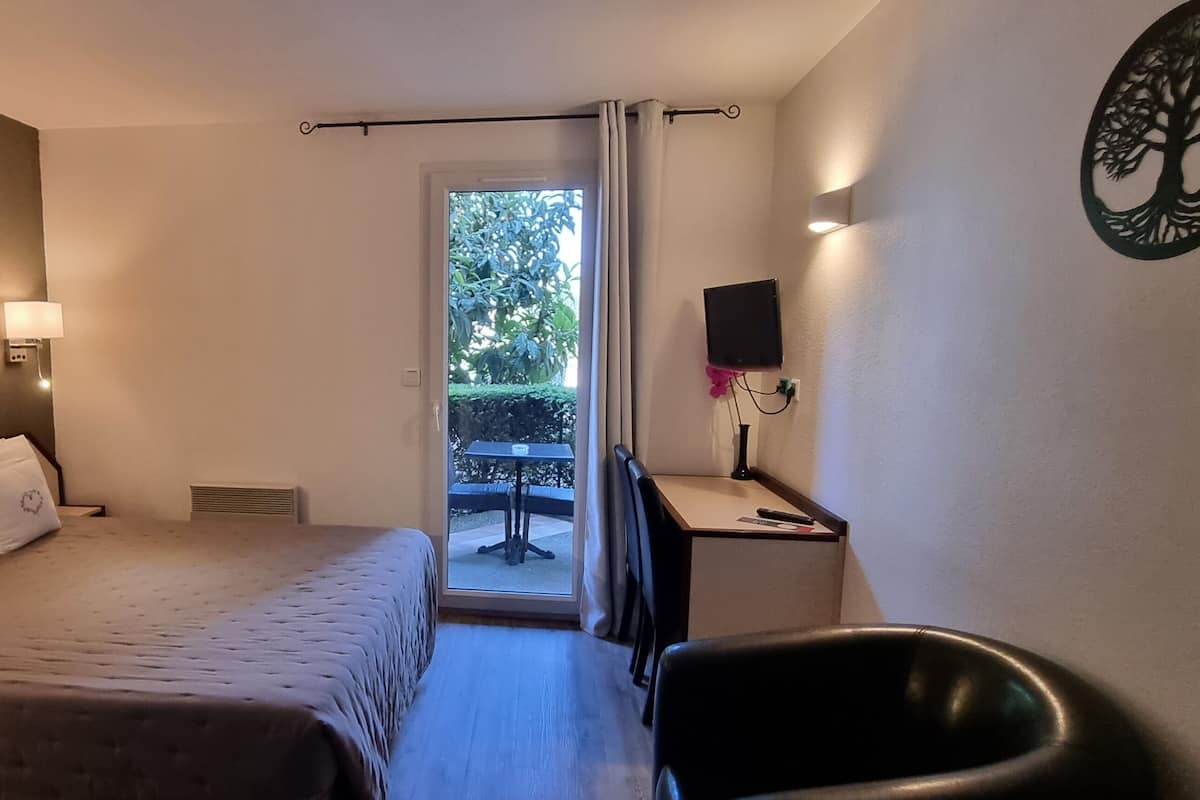 A hotel room with a bed, bedside table, chair, and a view of the outdoors.