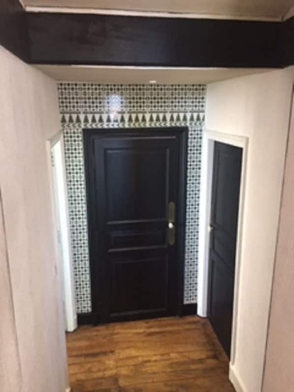 A hallway with a dark wooden door, patterned tile walls, and a wooden floor.