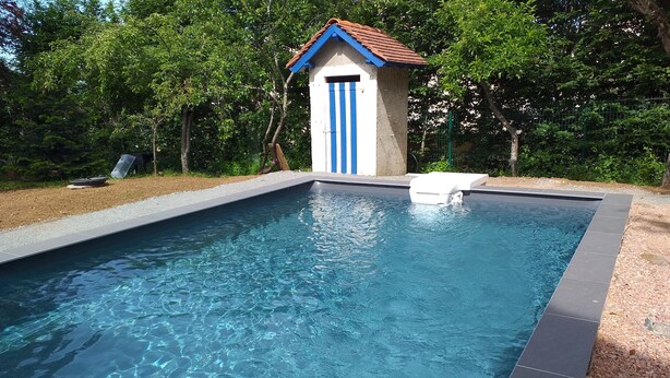 Ein rechteckiger Pool mit einer gefliesten Kante und einem kleinen Bauwerk mit einer blauen Tür im Hintergrund.