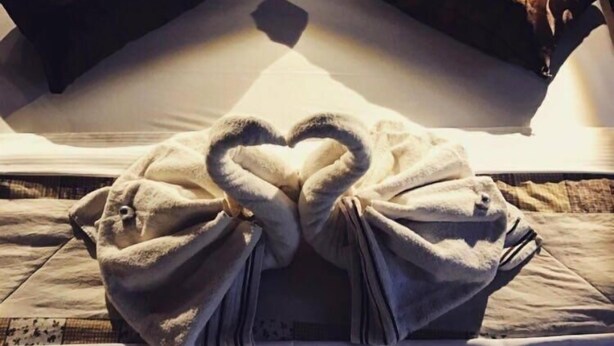 A bed with pillows arranged in a heart shape and a blanket folded into a heart.