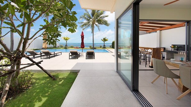 Ein modernes Haus mit Glastür zu einem Essbereich, einem Pool mit Liegestühlen und Blick aufs Meer.