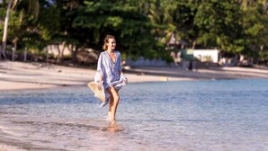 Eine Strandansicht mit klarem Wasser und einer Person, die am Strand entlangspaziert.