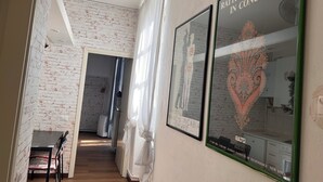 Un couloir avec un mur en briques, un coin repas avec une table et des chaises, et deux affiches encadrées accrochées au mur.