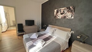 Une chambre à coucher moderne, avec un lit, des tables de chevet, un téléviseur et une œuvre d’art murale.