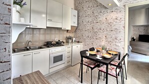 Une cuisine moderne avec des meubles blancs, une table à manger avec des chaises et un mur décoré d’un motif en briques.