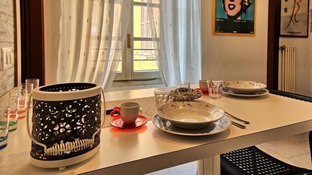 Un coin repas avec une table dressée pour deux personnes, agrémenté d’un vase noir et blanc à motifs, d’une tasse rouge et d’une assiette ornée de motifs floraux.