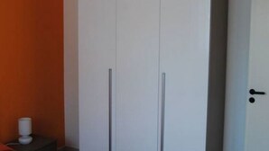 Een kamer met een witte garderobe, een tafeltje met een lamp en een deur met een zwarte knop.