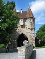 Um castelo de pedra com um arco central, rodeado por vegetação e um caminho de pedras.