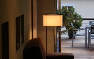 Quarto com abajur, poltrona e vista para área externa com mesa e cadeiras.