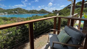 Un balcon donnant sur une zone côtière, avec vue sur une étendue d’eau où se trouvent des bateaux et, au loin, un bâtiment.