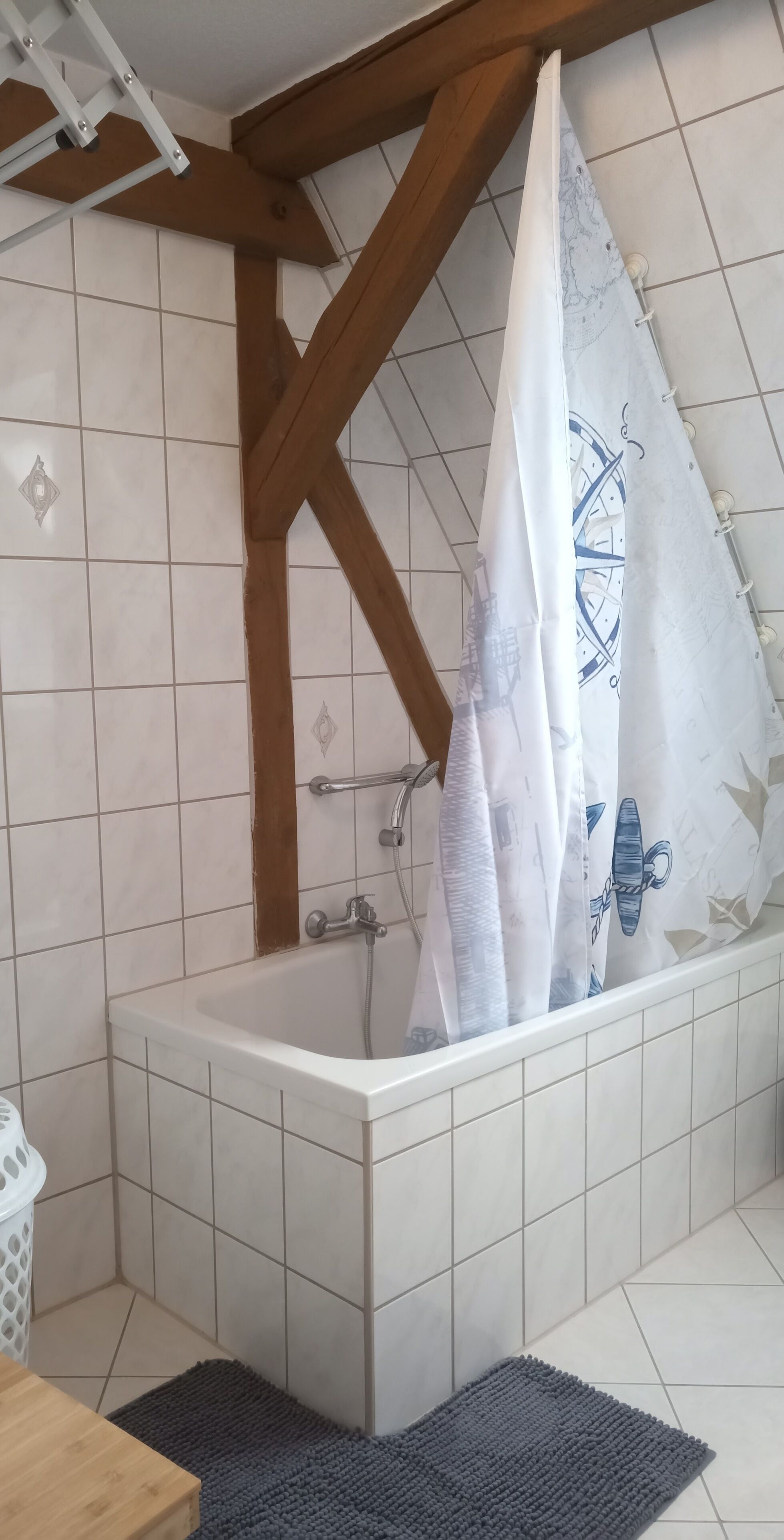 A bathroom with a bathtub, tiled walls, wooden beams, and a shower curtain with a nautical design.