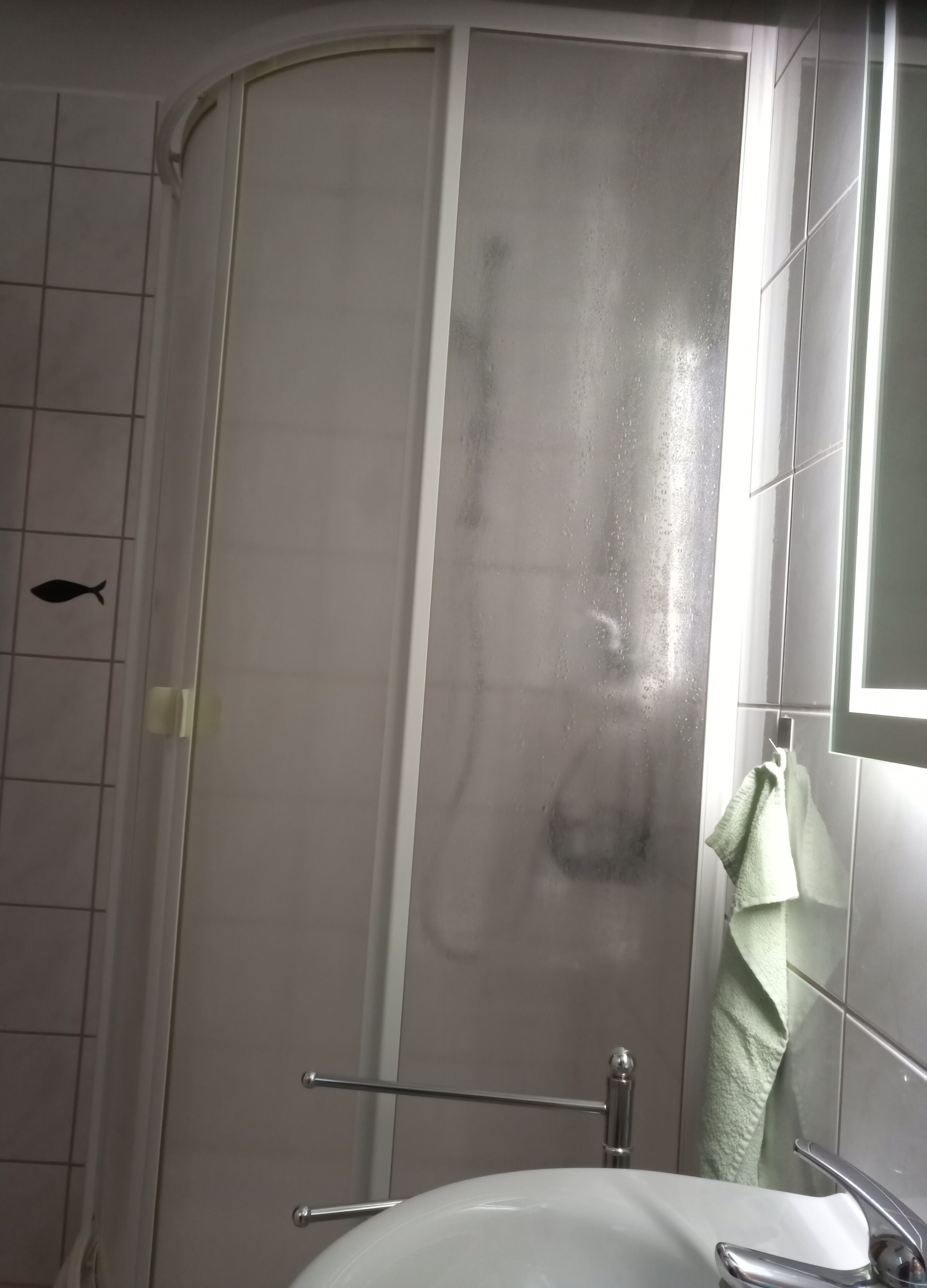A bathroom with a glass shower enclosure, a white sink, and a towel hanging on the wall.