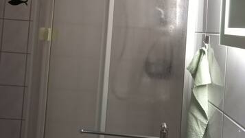A bathroom with a glass shower enclosure, a white sink, and a towel hanging on the wall.