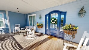 Une véranda avec une porte bleue, des fauteuils à bascule blancs et des plantes en pot.