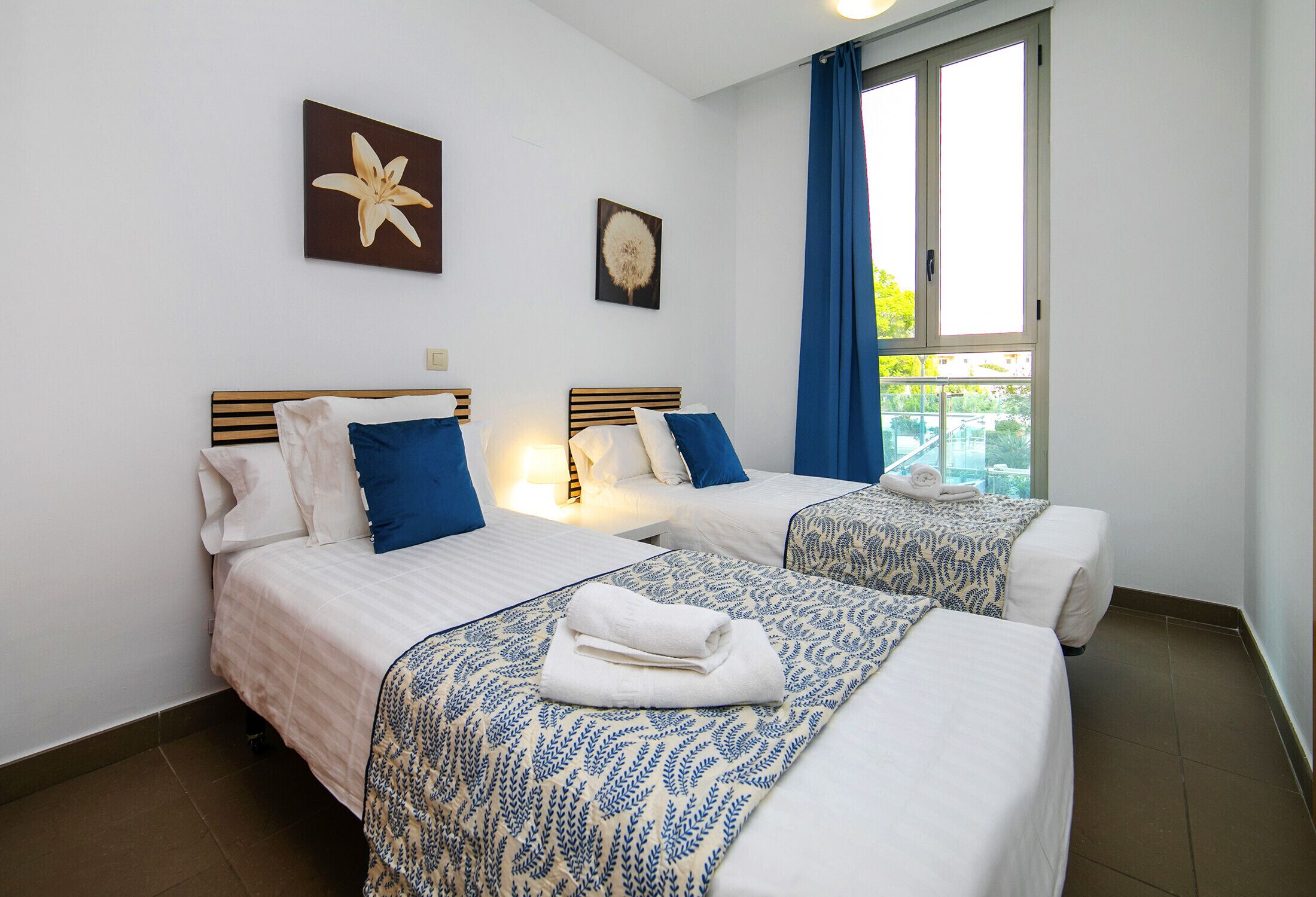 Une chambre d’hôtel avec deux lits, une fenêtre avec des rideaux et des œuvres d’art accrochées aux murs.
