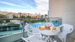 A balcony with a table set for breakfast, a pool in the background, and a cityscape view. - Borumbot 8.0.3 Vista Piscina (Calpe)
