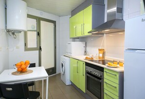 A compact kitchen with a washing machine, a stove, and a dining area with a table and chairs. - Borumbot 8.0.3 Vista Piscina (Calpe)