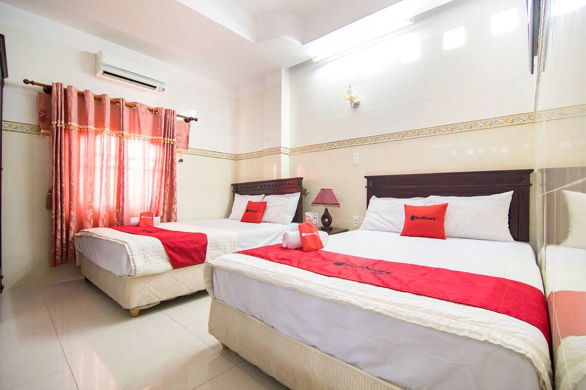 A hotel room with two beds, each with a red blanket and pillows, and a window with red curtains.
