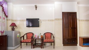 A living room with a TV mounted on the wall, two patterned chairs, a small table, a refrigerator, and a wooden cabinet. - RedDoorz Plus near Tan Son Nhat Airport (Ho Chi Minh City)