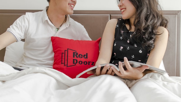 A couple sitting on a bed with a red pillow that has 'Red Doorz' printed on it. - RedDoorz Plus near Tan Son Nhat Airport (Ho Chi Minh City)