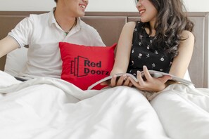 A couple sitting on a bed with a red pillow, reading a book. - RedDoorz Plus near Tan Son Nhat Airport (Ho Chi Minh City)