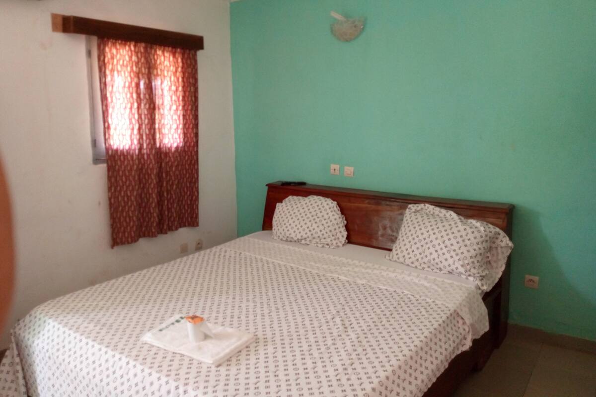 A bedroom with a bed, a window with curtains, and a wall-mounted light fixture.
