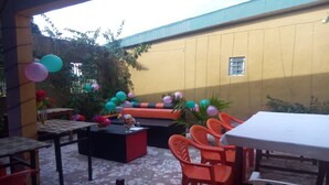 An outdoor patio area with a yellow wall, a sofa, orange chairs, and a table. - Residence Palace Hotel (Odienne)