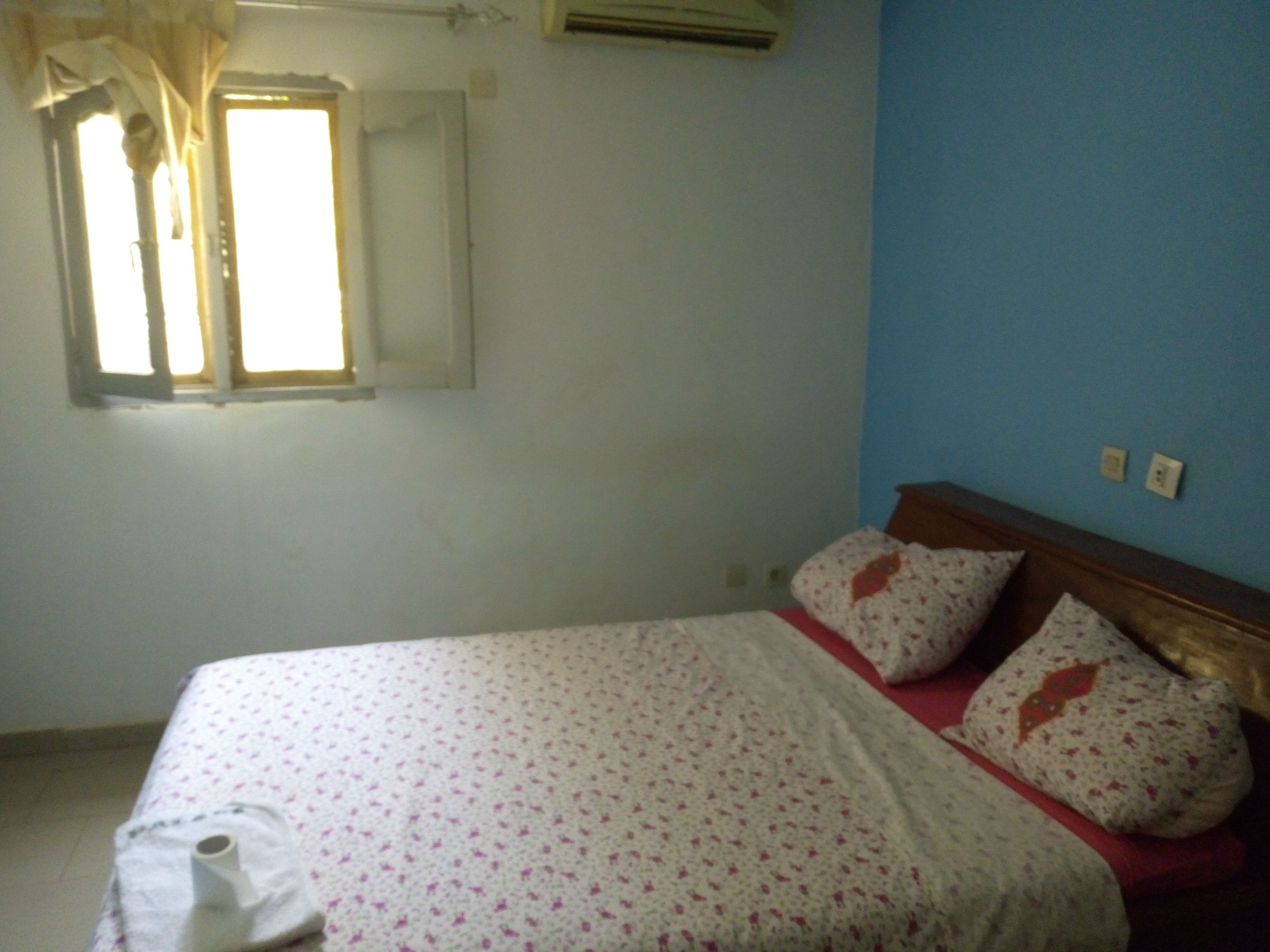Une chambre à coucher avec un lit, une fenêtre avec des rideaux et un climatiseur fixé au mur.