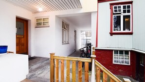 Una escalera conduce a un segundo piso con baranda de madera, un edificio rojo y blanco, y una motocicleta estacionada afuera.