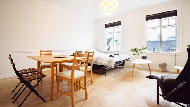 Una habitación con una mesa de comedor de madera, sillas, una cama, una mesita con una planta y un sillón de cuero negro.