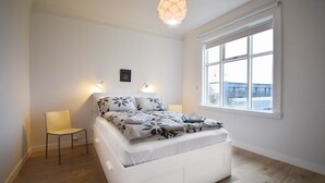 Un dormitorio con cama, una silla, un ventanal y una lámpara colgante.